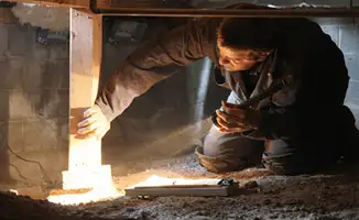 A professional inspecting wooden beams under the floor of a structure in Louisville, KY